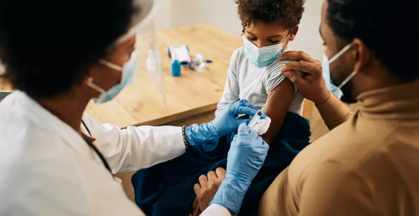 African American boy getting a vaccine while being with his father at pediatrician's office.